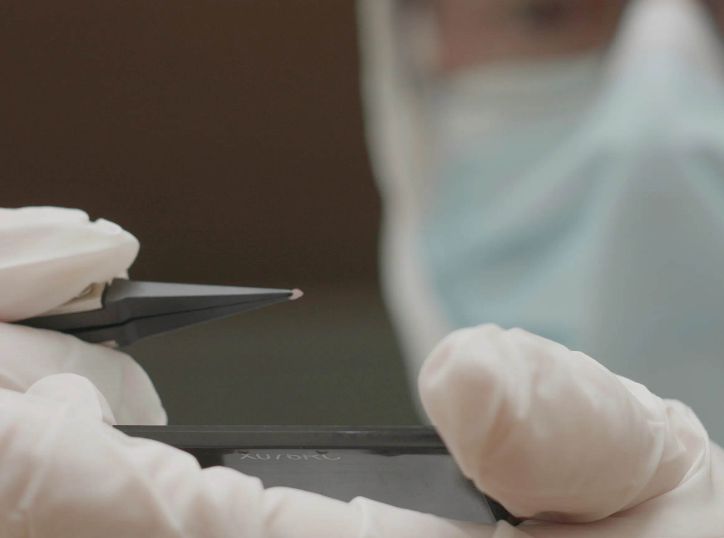 A researcher in a cleanroom holds a chip in front of them using a pair of tweezers.